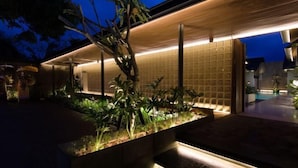 A modern outdoor area with a wooden pergola, a water feature, and a well-maintained garden. - Umahan Sanur (Bali)
