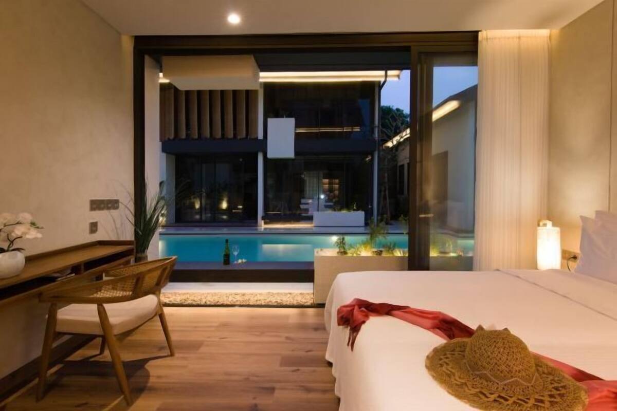 A modern hotel room with a large bed, a desk, a chair, and a view of a swimming pool.