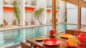 A modern indoor pool area with a dining table set for two, surrounded by lounge chairs and a wooden ceiling structure. - Hotel J, Unawatuna (Unawatuna)