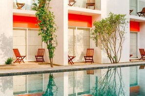 Un edificio moderno con piscina de vidrio, sillas de madera y plantas en macetas.