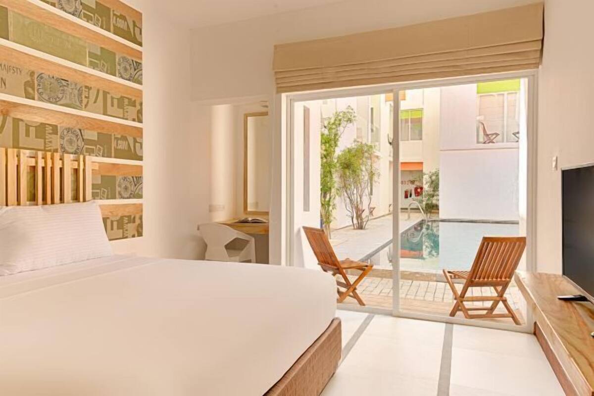 A hotel room with a bed, a desk, a TV, and a balcony with chairs.