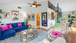 Un salón amplio con un sofá azul, una mesa de centro de cristal y una escalera que conduce a un nivel superior.