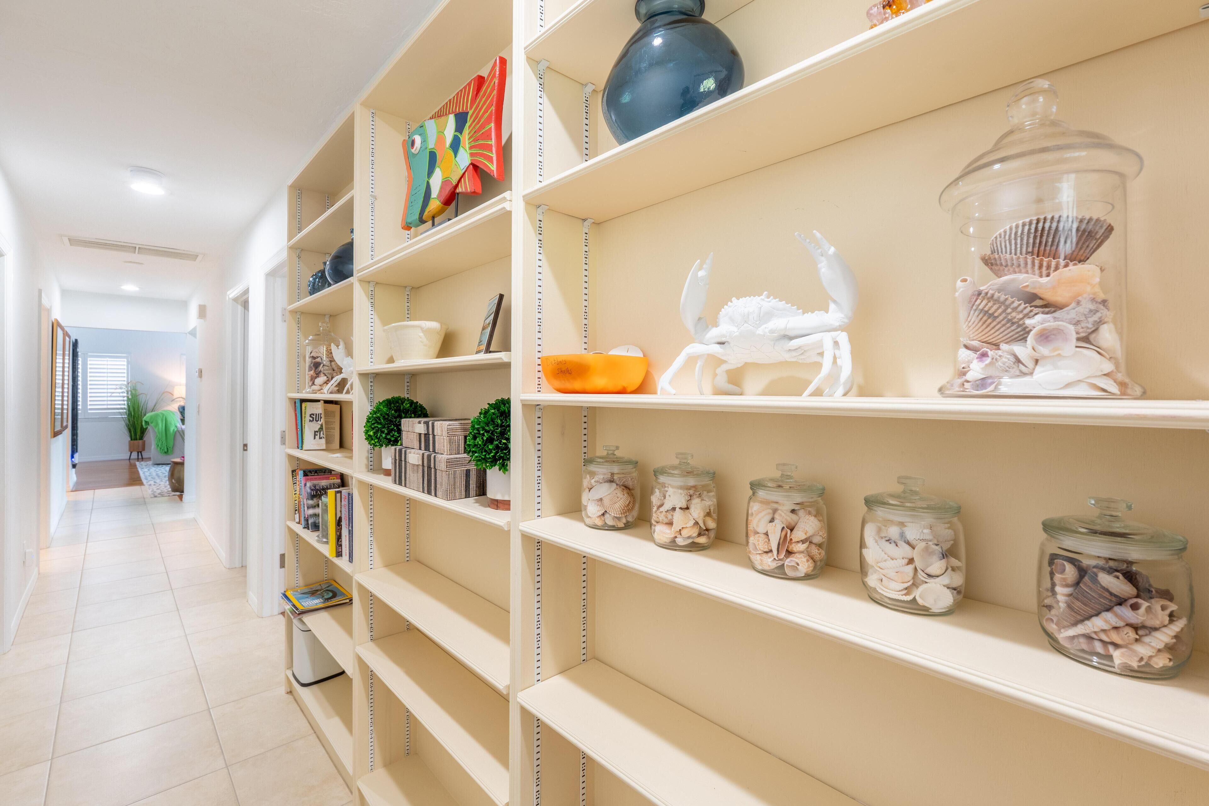 A hallway with shelves containing decorative items, including jars of seashells and a white crab sculpture.