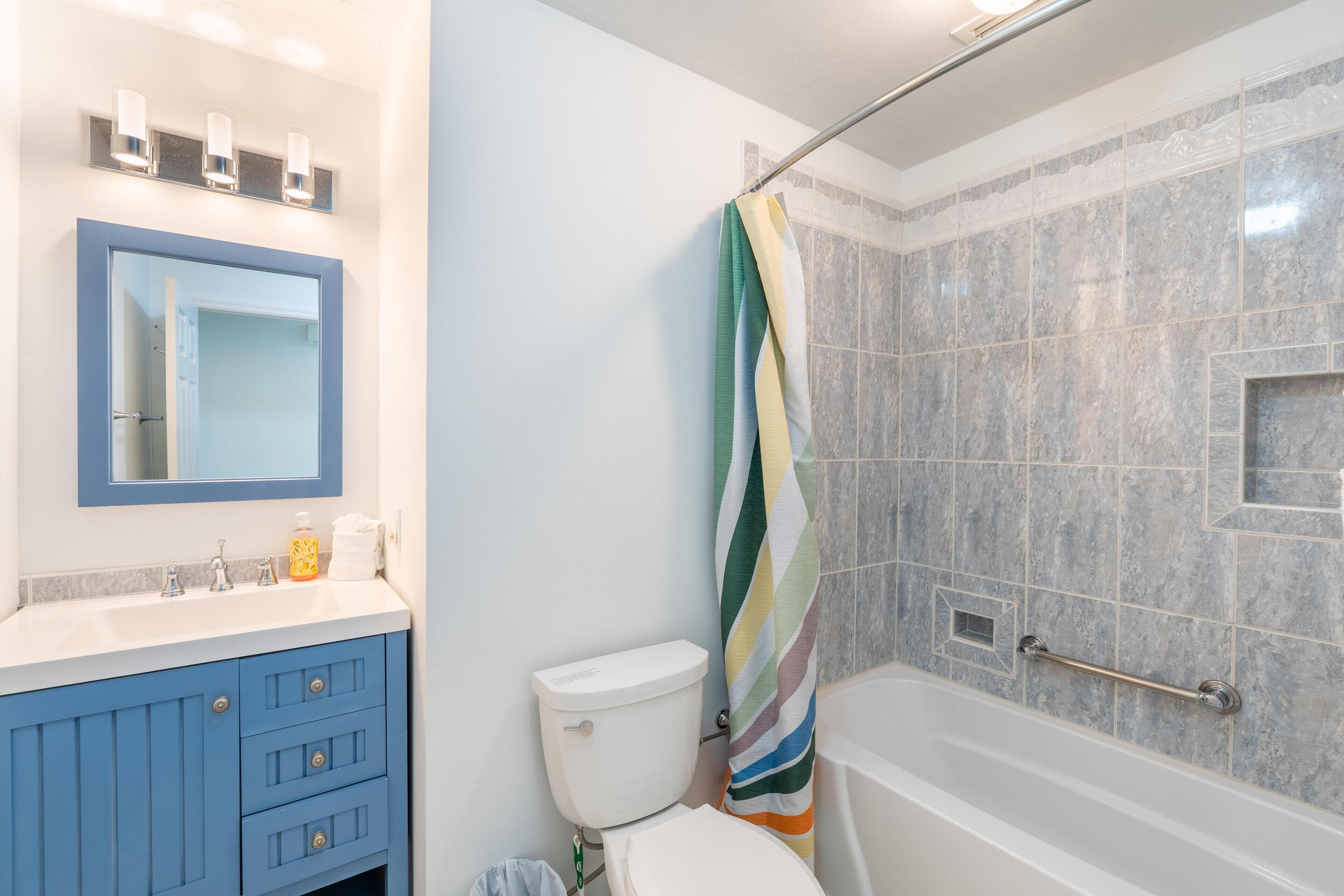 Une salle de bain avec un meuble-lavabo bleu, des toilettes, une douche avec un rideau à rayures et une baignoire.