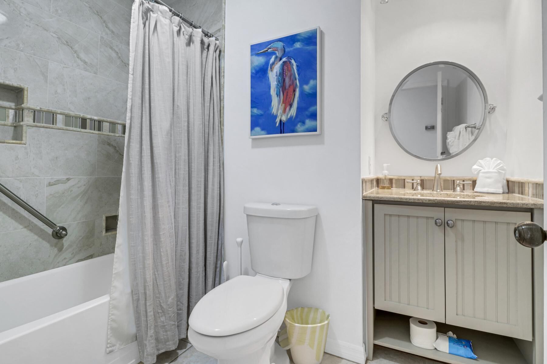 Une salle de bain équipée d’une douche, de toilettes, d’un lavabo et ornée d’un tableau représentant un oiseau.