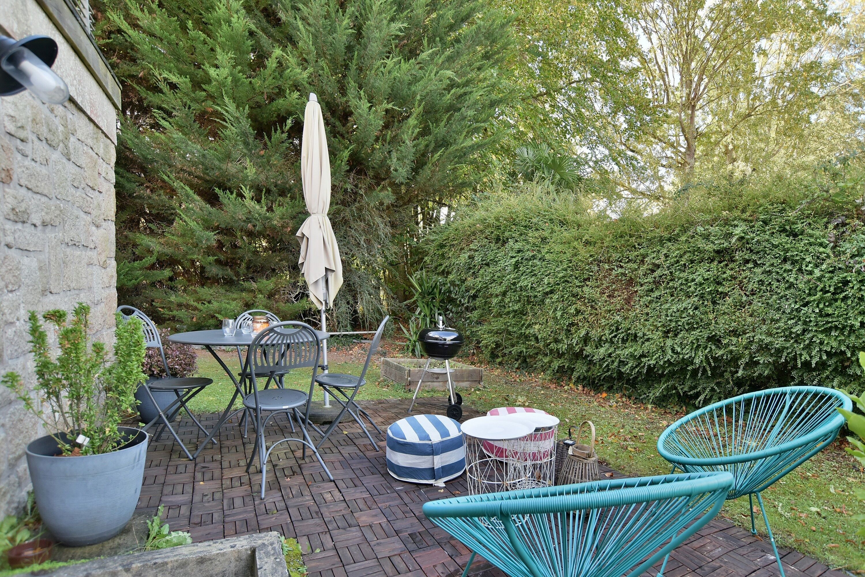 A patio area with a brick floor, outdoor furniture including chairs and tables, a potted plant, and a large umbrella.