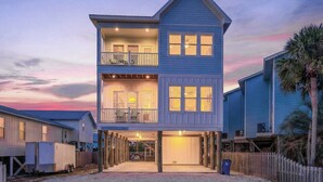 A two-story building with a balcony on the upper floor, a covered entrance, and a sign indicating it is a vacation rental. - Lux 6BR - Heated Pool | Sleeps 22 | 1 min to beach (Gulf Shores)