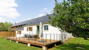 Ein zweistöckiges Haus mit einer Holzterrasse, einem Essbereich mit Gartenmöbeln und einer grünen Tür.