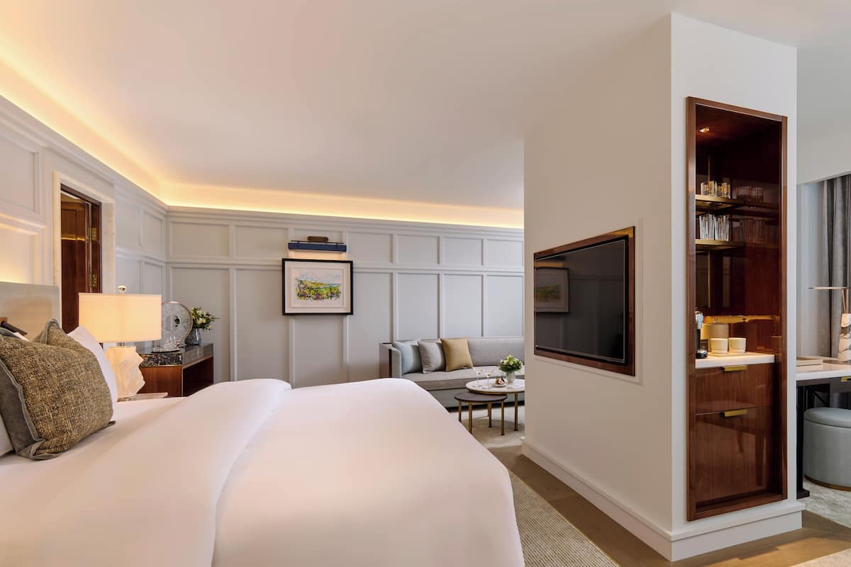 Habitación de hotel con una cama grande, un sofá, una mesita, un televisor y un vestidor.