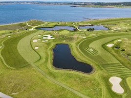 Vista aérea de un campo de golf con varios obstáculos de agua, búnkeres de arena y un gran estanque central.