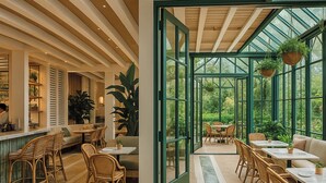 Ruime binnenruimte met een grote glazen deur die uitkomt op een tuin, ingericht met rieten stoelen en tafels.