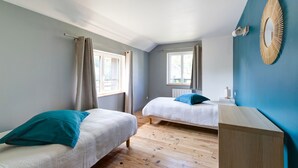 Un dormitorio con dos camas, suelo de madera, pared de acento azul y un espejo grande.