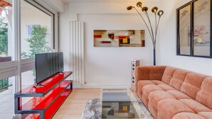 Una sala de estar moderna con un mueble multimedia rojo, un sofá, una mesa de centro de vidrio y un cuadro en la pared.