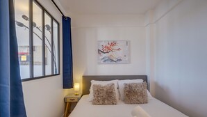 Una cama bien hecha con almohadas mullidas, una lámpara de noche y una obra de arte en la pared que representa un paisaje de montaña.