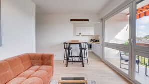 Una sala de estar moderna con un sofá, una mesita y una cocina al fondo.