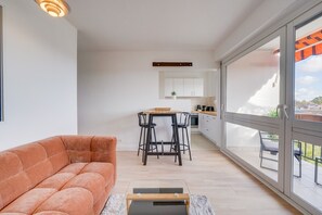 Ein modernes Wohnzimmer mit einer Couch, einem kleinen Tisch und einer Küche im Hintergrund.