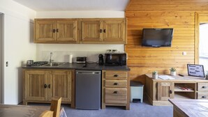 Cocina compacta con armarios de madera, lavavajillas, microondas y televisor montado en la pared.