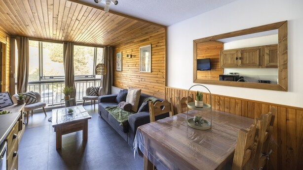 Una sala de estar acogedora con techo de madera, un sofá, una mesa de comedor y un gran ventanal con vistas al exterior.
