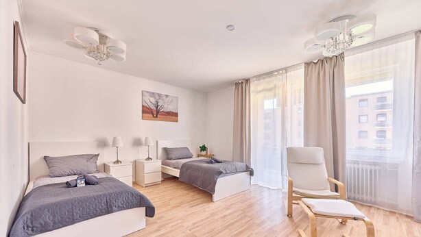 A modern hotel room with two beds, a sitting area with a chair, a view of the city, and a painting on the wall. - Ida - Bergheim near Cologne (Bergheim)