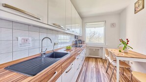 A modern kitchen with a black sink, wooden countertop, and white cabinets. There is a window with a view of trees and a clock on the wall. - Ida - Bergheim near Cologne (Bergheim)