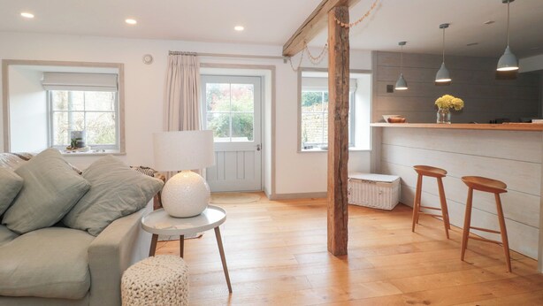 Una sala de estar acogedora con un sofá, una mesa redonda con una lámpara, y una zona de cocina con taburetes y luces colgantes.