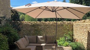 Un espacio de patio con un sofá color beige, dos mesitas auxiliares y un paraguas grande color beige.