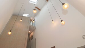 Un interior moderno con vigas de madera a la vista, tragaluces y lámparas colgantes.