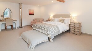 Un dormitorio con cama, mesitas de noche, un escritorio, una silla, un espejo y una obra de arte colgada.