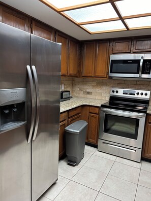 Eine Küche mit einem Edelstahl-Kühlschrank, einer Mikrowelle, einem Backofen und einem Mülleimer.
