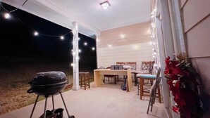 Une terrasse extérieure équipée d’un barbecue, d’une table à manger avec des chaises et de guirlandes lumineuses.