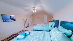 Une chambre avec deux lits, un ventilateur de plafond, un téléviseur fixé au mur et une porte visible au fond.