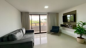A modern living room with a sofa, a chair, a TV, and a potted plant. - Gold Flat  (João Pessoa)