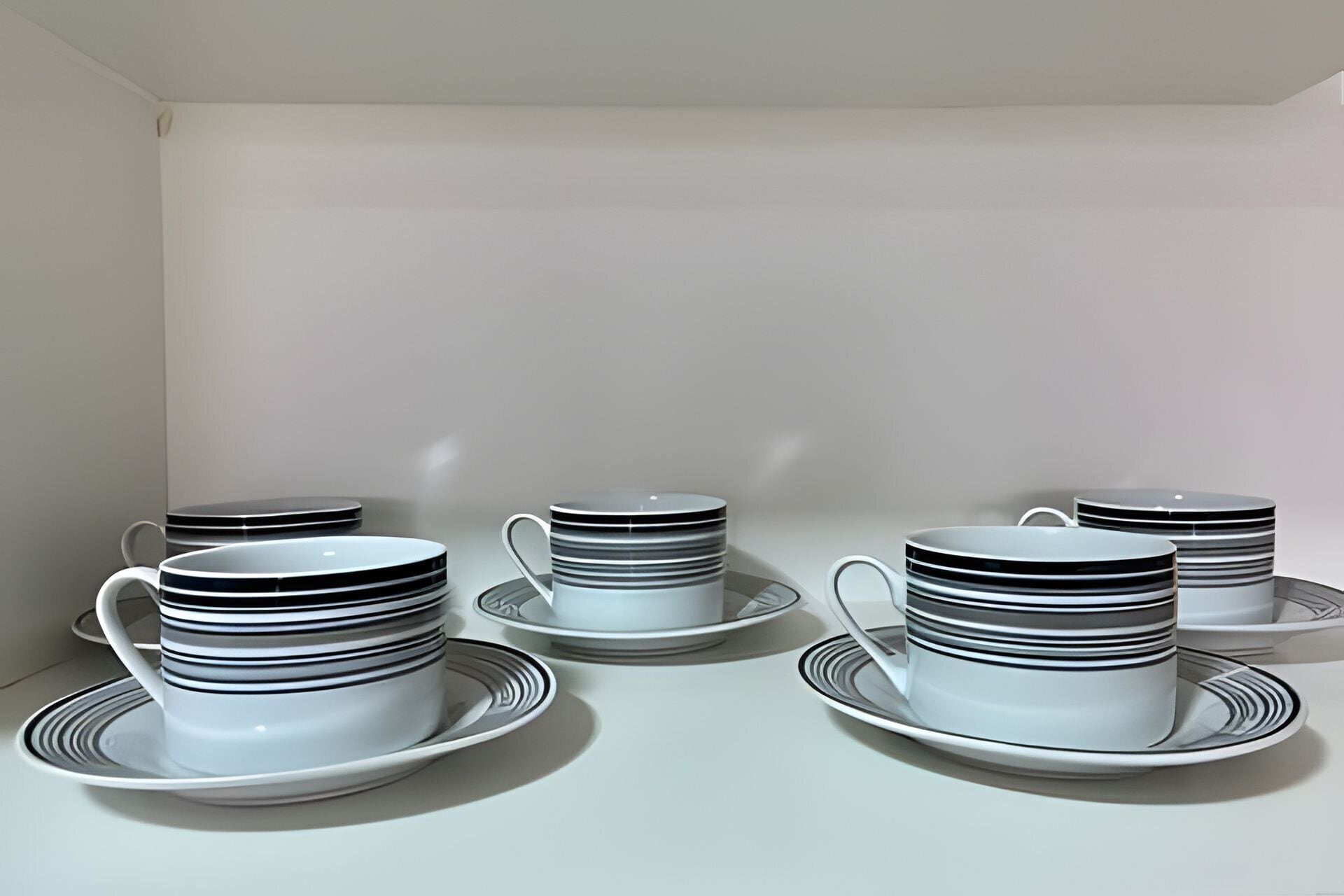 A set of white and black striped cups and saucers arranged on a table against a plain wall.