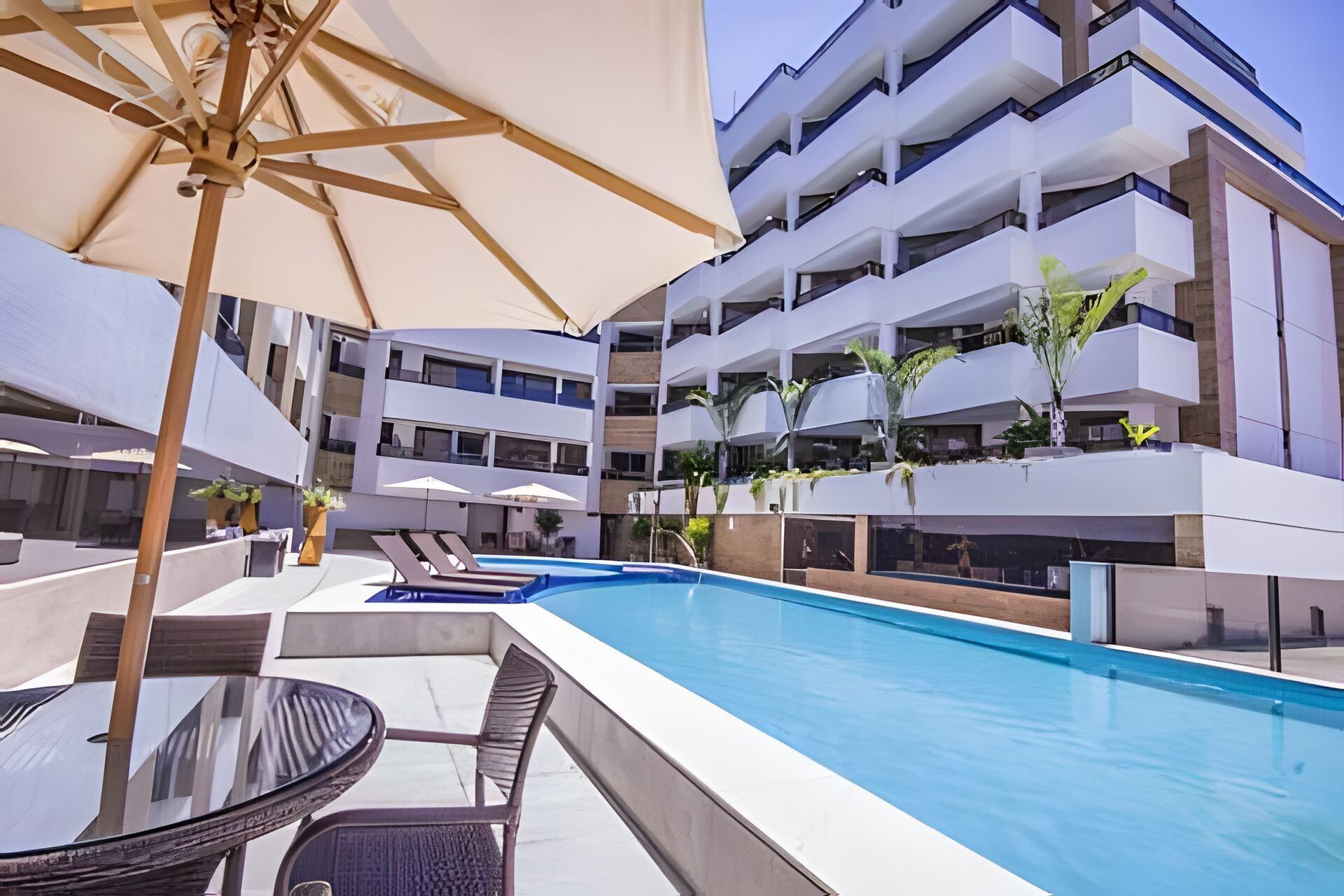 A modern hotel with a swimming pool, lounge chairs, and umbrellas.