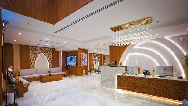 A hotel reception area with a marble floor, a reception desk, a seating area with a sofa, and a television screen. - Seagull Apartment Service (Jeddah)