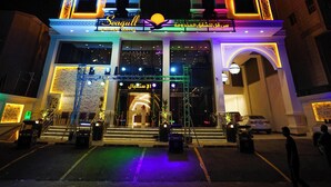 A hotel with a modern facade, illuminated by colorful lights, featuring a prominent entrance with a glass door and a staircase leading up to the entrance. - Seagull Apartment Service (Jeddah)