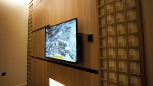 A hotel room with a television mounted on a wooden panel, a bench with a cushion, and a patterned floor. - Seagull Apartment Service (Jeddah)