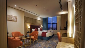 A hotel room with a bed, two orange chairs, a small table, a desk, and a TV. - Seagull Apartment Service (Jeddah)