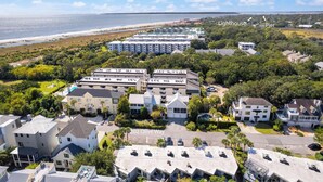 Luchtbeeld van een kustgebied met woonhuizen, waaronder een opvallend wit gebouw met balkon en een kleinere constructie met garage.