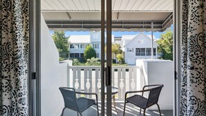 Een balkon met twee stoelen en een tafel, wit hekwerk, en uitzicht op huizen en groen.