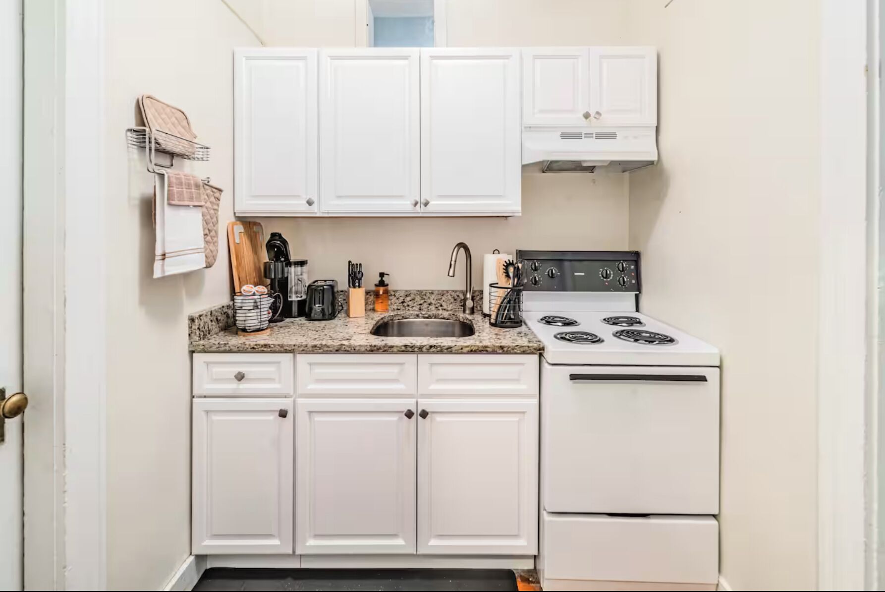 A small kitchen with white cabinets, a granite countertop, a stove, and a sink.