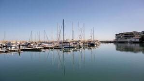 A marina with multiple sailboats docked at calm water, a clear sky, and a building with balconies on the right. - Boardwalk Bliss Explore the Lively Mindarie Marina (Mindarie)