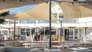 An outdoor seating area with tables and chairs under large umbrellas, a building with a glass facade in the background, and a clear sky. - Boardwalk Bliss Explore the Lively Mindarie Marina (Mindarie)