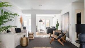 Un salon moderne avec un canapé, un fauteuil et une table basse. On y trouve également une grande plante et un cactus.