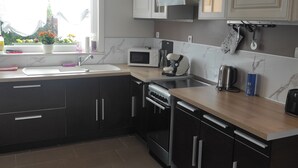 A modern kitchen with dark cabinets, a microwave, stove, and a window with a view of greenery. - L'essentiel en campagne (Calais) Farmhouse 10 minutes from the beach! Private Parking! (Guemps)
