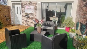 An outdoor seating area with wicker furniture and artificial grass, a brick wall, and a sliding glass door leading to an indoor space. - L'essentiel en campagne (Calais) Farmhouse 10 minutes from the beach! Private Parking! (Guemps)