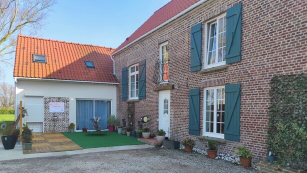 A two-story brick building with green shutters, a red-tiled roof, and a small garden area with potted plants. - L'essentiel en campagne (Calais) Farmhouse 10 minutes from the beach! Private Parking! (Guemps)