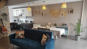 A modern living room with a blue sofa, kitchen in the background, and decorative wall art. - L'essentiel en campagne (Calais) Farmhouse 10 minutes from the beach! Private Parking! (Guemps)