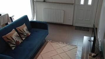 Una sala de estar con sofá azul, cojín decorativo estampado, alfombra color beige, espejo en la pared y puerta blanca.