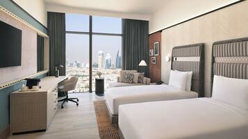 A hotel room with two beds, a desk, a TV, and a large window offering a city view.